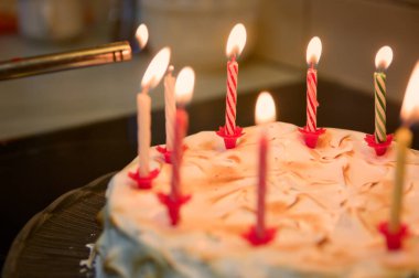 Closeup of a birthday cake being decorated with lit candles using a kitchen burner