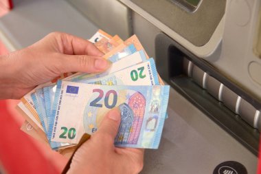 Bir kadının elleri bankadaki ATM 'nin önünde bir kaç avroluk banknot tutuyor.