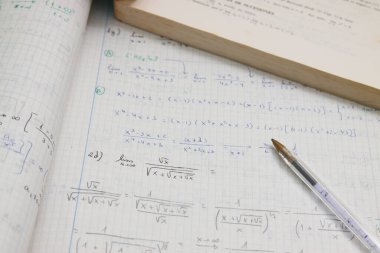 Bir kalem ve öğrenci kitabının yanında ileri matematik ödevi (limitler) bulunan bir defterin resmi