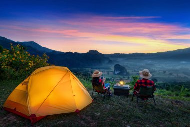 Romantik çift dışarıda kamp yapıyor ve gün doğumunda kamp yaparken kamerayla fotoğraf çekiyor. Phu Lang Ka, Pha yao bölgesi Tayland.