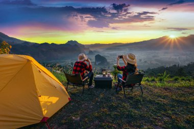 Romantik çift dışarıda kamp yapıyor ve gün doğumunda kamp yaparken kamerayla fotoğraf çekiyor. Phu Lang Ka, Pha yao bölgesi Tayland.