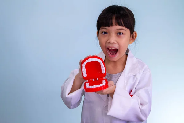 Yakışıklı Asyalı çocuk doktor dişçi oyuncak setiyle oynuyor, çocuk dişleri nasıl temizleyeceğini ve bakacağını gösteriyor. Diş hekimliği ve ilaç,