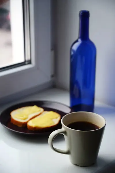 bottle, cup of coffee  and toasts on windowsill