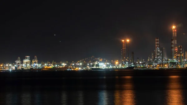 Oil refinery plant at night. Long exposure of factory lights reflection on sea. Noise and grain included