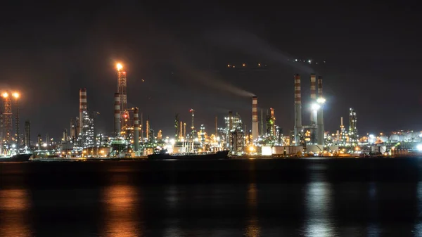 Oil refinery plant at night. Long exposure of factory lights reflection on sea. Noise and grain included