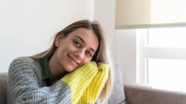 Beautiful smiling woman with blonde hair and green eyes looking at camera. Woman wearing sweater at home in winter day. Girl on cozy mood relaxing at home. International Womens day for 8th March