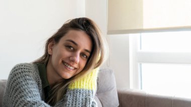 Young beautiful woman wearing comfortable and warm clothes at home in winter day. Happy woman relaxing at home