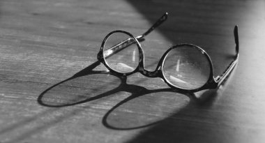 Glasses on wooden table. Sunshine reflecting on vintage glasses on the table. Wisdom concept. Copy space for text. Black and white backgroun