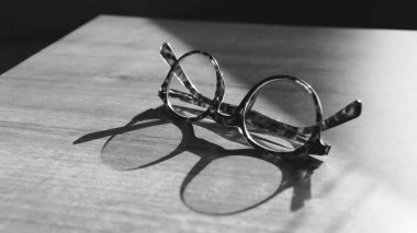 Glasses on wooden table. Sunshine reflecting on vintage glasses on the table. Wisdom concept. Copy space for text. Black and white backgroun