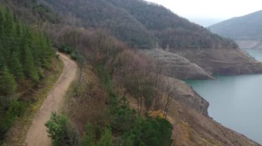 Walking path in a forest by the lake aerial view. dam and forest footage in misty weather.