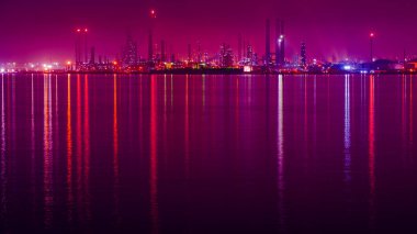 Geceleri petrol rafinerisi. Petrol rafinerisi ışıkları denize yansıyor. Gece manzarası, uzun pozlu fotoğrafçılık. Seçici odak dahil