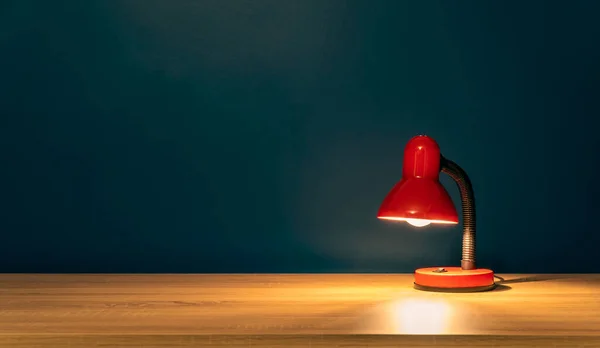 Study concept background. Desk lamp on a wooden table. Work from home concept. Red desk lamp on a table with copy space fot text. Blank area on a wooden table