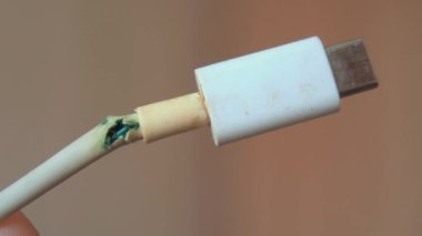 Eski şarj kablosu kırılmış, yakın plan beyaz yalıtım malzemesi. Arızalı şarj kablosu, bozulan cihaz bağlantısı. Tehlike, yangın güvenliği, kısa devre.