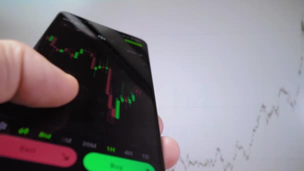 ビジネスマントレーダー投資家アナリストは 携帯電話アプリケーションを使用して暗号通貨金融市場 スマートフォン上の取引データのチャートインデックスを分析します バックグラウンドでグラフが表示されます — ストック動画