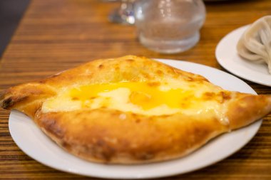 Adjarian Khachapuri 'nin bir restoranda beyaz bir tabakta yakın çekimi. Geleneksel Gürcü mutfağı. Seçici odak