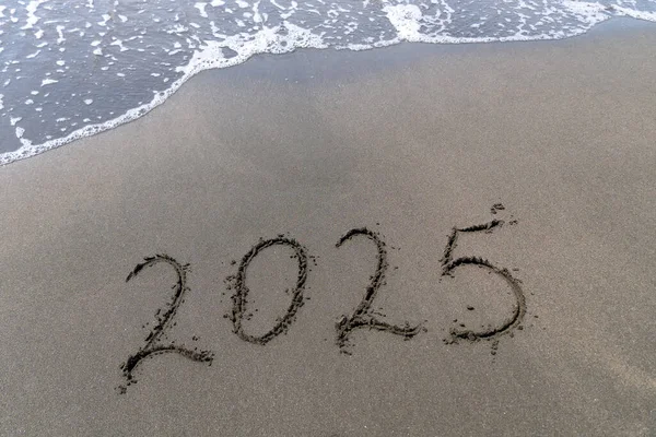 Text Happy New Year 2025 on a sandy sea beach with a small wave. Abstract background photo of the upcoming New Year 2023