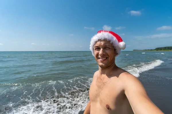 Lächelnder Mann Mit Nikolausmütze Macht Vor Dem Hintergrund Des Meeres — Stockfoto