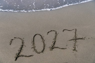 Küçük bir dalgayla kumlu bir sahilde mutlu yıllar 2027 mesajı at. Gelecek Yeni Yıl 2023 'ün soyut arka plan fotoğrafı