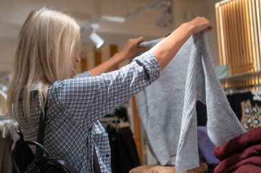 Güzel genç bayan alışverişçi bir giyim mağazasından alışveriş yapıyor, şık kıyafetler seçiyor. Moda mağazasındaki insanlar. Yeni mevsimlik koleksiyon.
