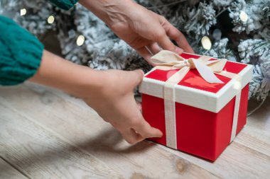 Yeşil kazaklı bir kadın eli ya da Noel ağacının altına kırmızı bir hediye kutusu. Noel ve Yeni Yıl kavramı