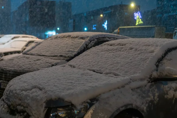 Close-up of snow-covered hoods of cars standing in a row in the parking lot on a snowy evening