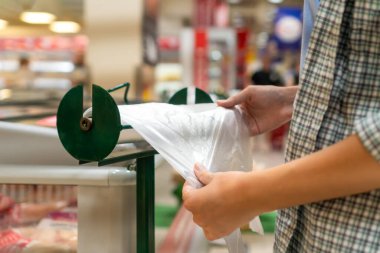 Bir markette paketlemek için biyolojik olarak çözünebilen bir selofan poşeti yırtan kadın ellerine yakın plan.