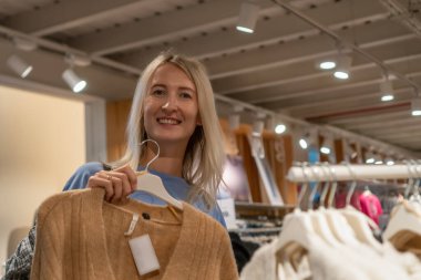 Güzel genç bayan alışverişçi bir giyim mağazasından alışveriş yapıyor, şık kıyafetler seçiyor. Moda mağazasındaki insanlar. Yeni mevsimlik koleksiyon.