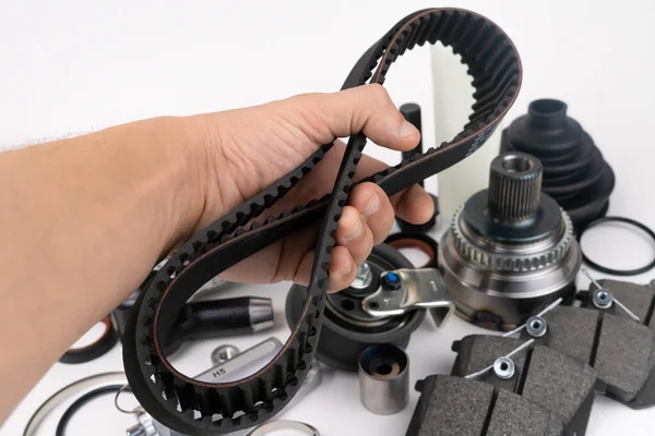 Timing belt and tension rollers of gas distribution system of car engine, concept of car maintenance. Master\'s hand holds timing belt against background of spare parts on white background