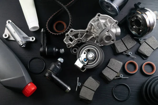 stock image Lot of auto parts lie on wooden black background. Engine and suspension parts, swivel knuckle, joint and engine parts unfolded. New spare parts. Bearings . Play by light. Hanging on table.