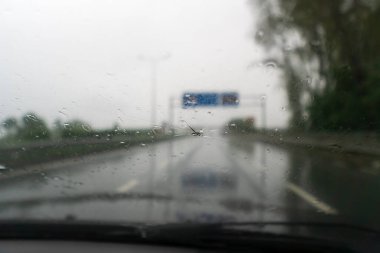 Yağmurlu bir havada uçan bir taşın kırdığı arabanın ön camı. Bardaktaki delik, cips ve molozlar, şeritlerdeki çatlaklar. Yağmur damlalarıyla taşa çarptığı için ön camı hasar görmüş bir araba.