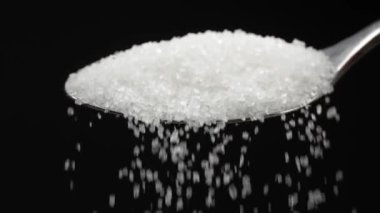 Sugar spoon full of powdered sugar crystals in teaspoon side view, filled with sugar for cooking and baking needed for drinks - coffee or tea is poured in slow motion close-up.