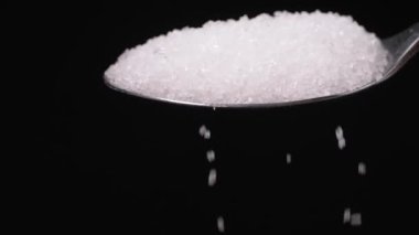 Sugar spoon full of powdered sugar crystals in teaspoon side view, filled with sugar for cooking and baking needed for drinks - coffee or tea is poured in slow motion close-up.