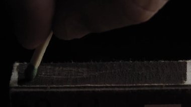 Matchstick light up after hitting flint surface of matchbox. Everything is real, no flame filters. Match moves on side of matchbox and light fire. Macro photography. slow motion.