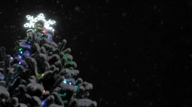 Christmas tree view of bottom against background of falling snow and black night sky. Christmas Eve and New Year's Eve, fir tree with glowing snowflake on top. Fabulous atmosphere.