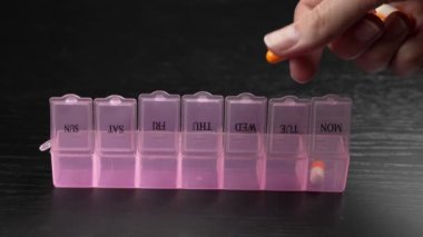Woman's hand puts pills for week in pill dispenser. Concept of health care and medicines. course of treatment for week. . Storing scheduled doses of medications in box.
