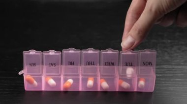 Woman's hand puts pills for week in pill dispenser. Concept of health care and medicines. course of treatment for week. . Storing scheduled doses of medications in box.