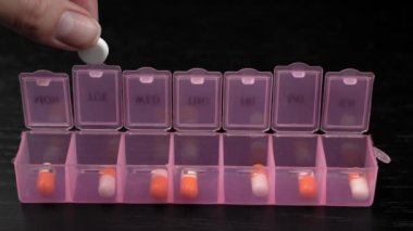 Woman's hand puts pills for week in pill dispenser. Concept of health care and medicines. course of treatment for week. . Storing scheduled doses of medications in box.