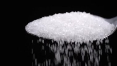 Sugar spoon full of powdered sugar crystals in teaspoon side view, filled with sugar for cooking and baking needed for drinks - coffee or tea is poured in slow motion close-up.