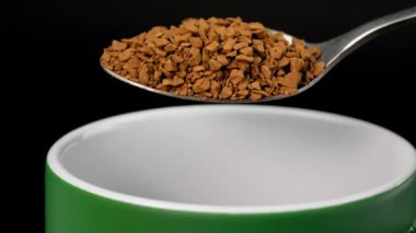 Instant coffee. Coffee powder product. Freeze-dried Instant coffee in spoon is added and poured in super slow motion on black background into green cup. Macro close-up. Caffeine.
