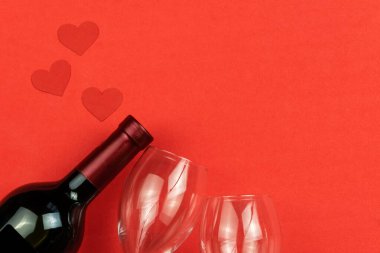 Bottle of wine, glasses hearts on a red background with copy space, top view. Concept of Valentine's day, love, festive dinner