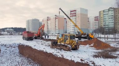 construction of new residential district with apartment buildings and new city highway. big city construction site. aerial top down view. Excavator loads dump truck with earth on winter day.