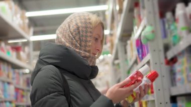 Kadın, ev için kozmetik ya da ev yapımı kimyasalları seçiyor. Ceketli güzel sarışın elinde bir şişe sıvı tutuyor. Yan görüş. Kişisel bakım ve modern kozmetoloji.