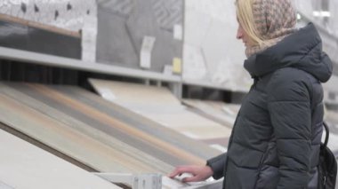 home repair. portrait of attractive woman in building shop chooses wooden laminated surface for home renovation and new design ideas One girl checks and feels large chipboard in store.