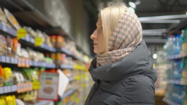 Blonda Frumoasă Uită Unele Rafturi Din Supermarket Încercând Decidă Cumpere — Videoclip de stoc