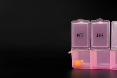Kapsülleri ve tabletleri siyah bir masanın üzerinde, makro fotoğrafçılığın olduğu açık pembe bir hap kutusunun yakın çekimi. Sağlıklı yaşam tarzı ve ilaç kavramı