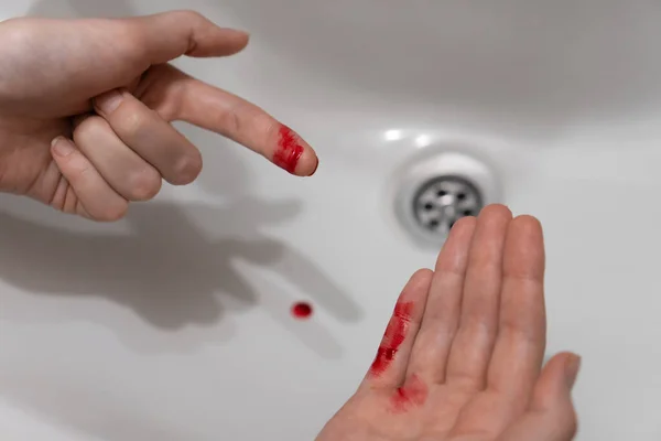 Close-up of a woman\'s cut finger in blood over the sink