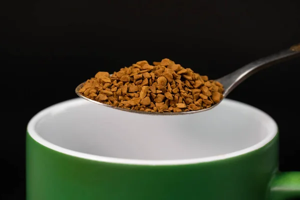 stock image Close-up of a teaspoon with granulated instant coffee over a mug, macro.