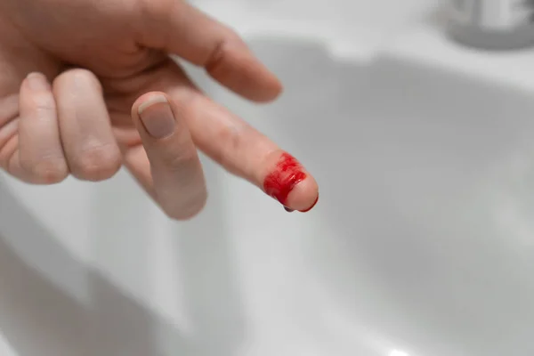 Close-up of a woman\'s cut finger in blood over the sink