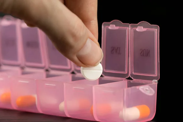 Macro photography a woman takes pills out of a pink pillbox with her hand or sorts pills and vitamins for daily medication on a black table. Concept of healthcare, medicine