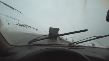 Dağlarda karla kaplı yolda araba sürerken kamera görüntüsü. - Evet. Direksiyondaki araba sürücüsünün elleri, kışın araba sürmek. Yukarı Lars 'a nakliye. Silecek operasyonu, görüş mesafesi zayıf. Tehlikeli bir şekilde..